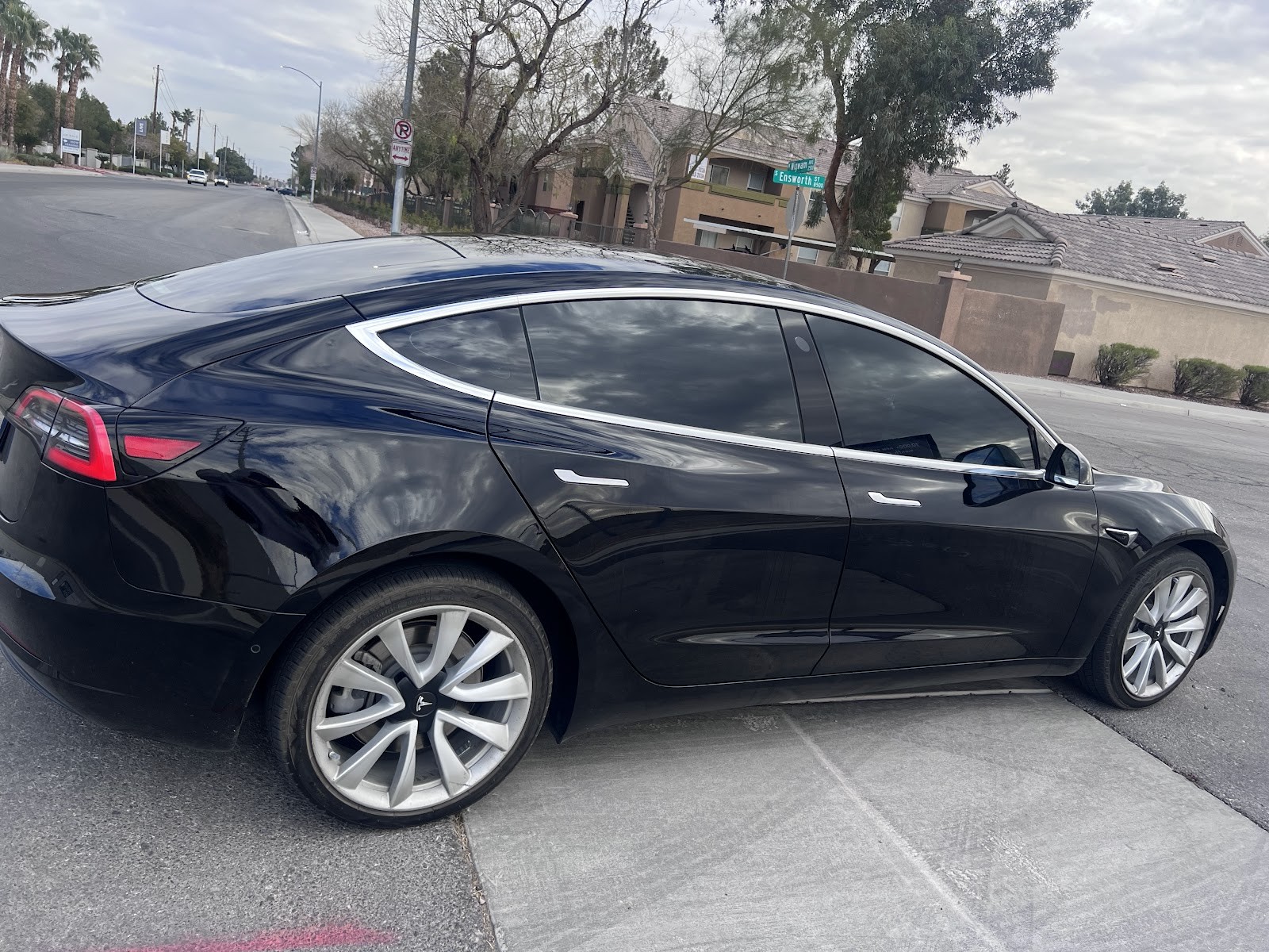 Black Tesla Model 3 with tinted windows parked at a residential street corner