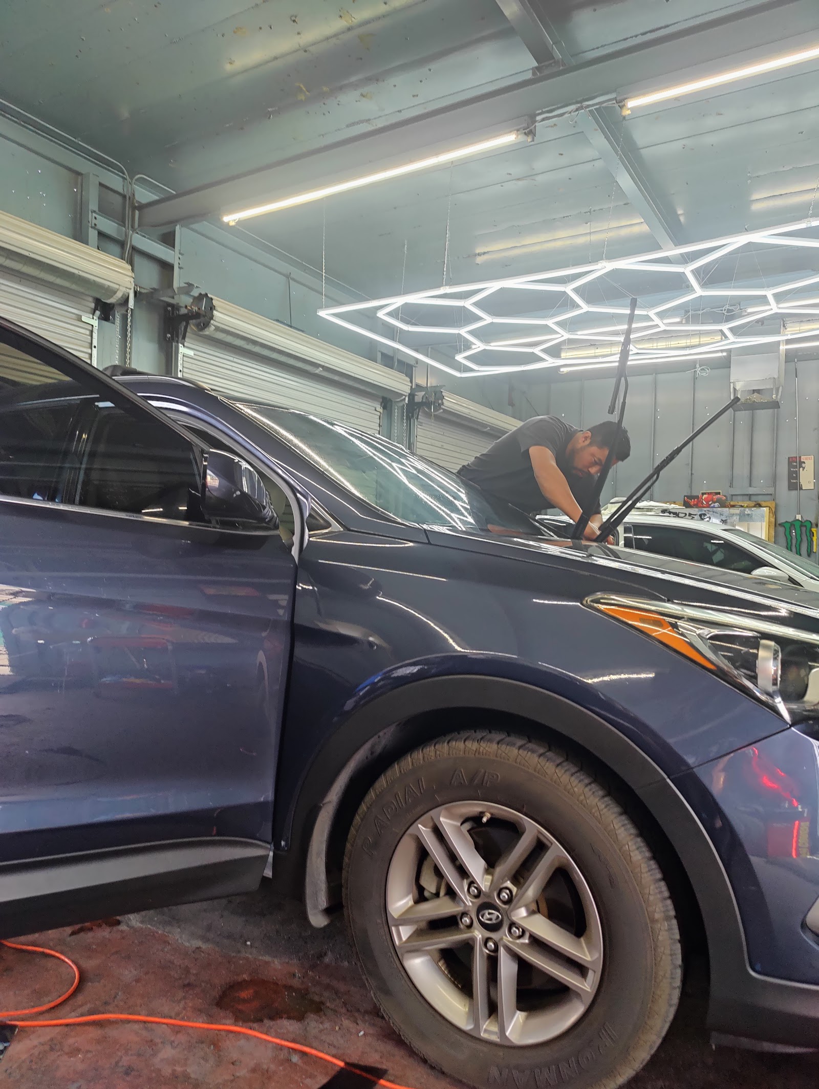 Technician installing window tint on the windshield of a blue Hyundai SUV inside the shop