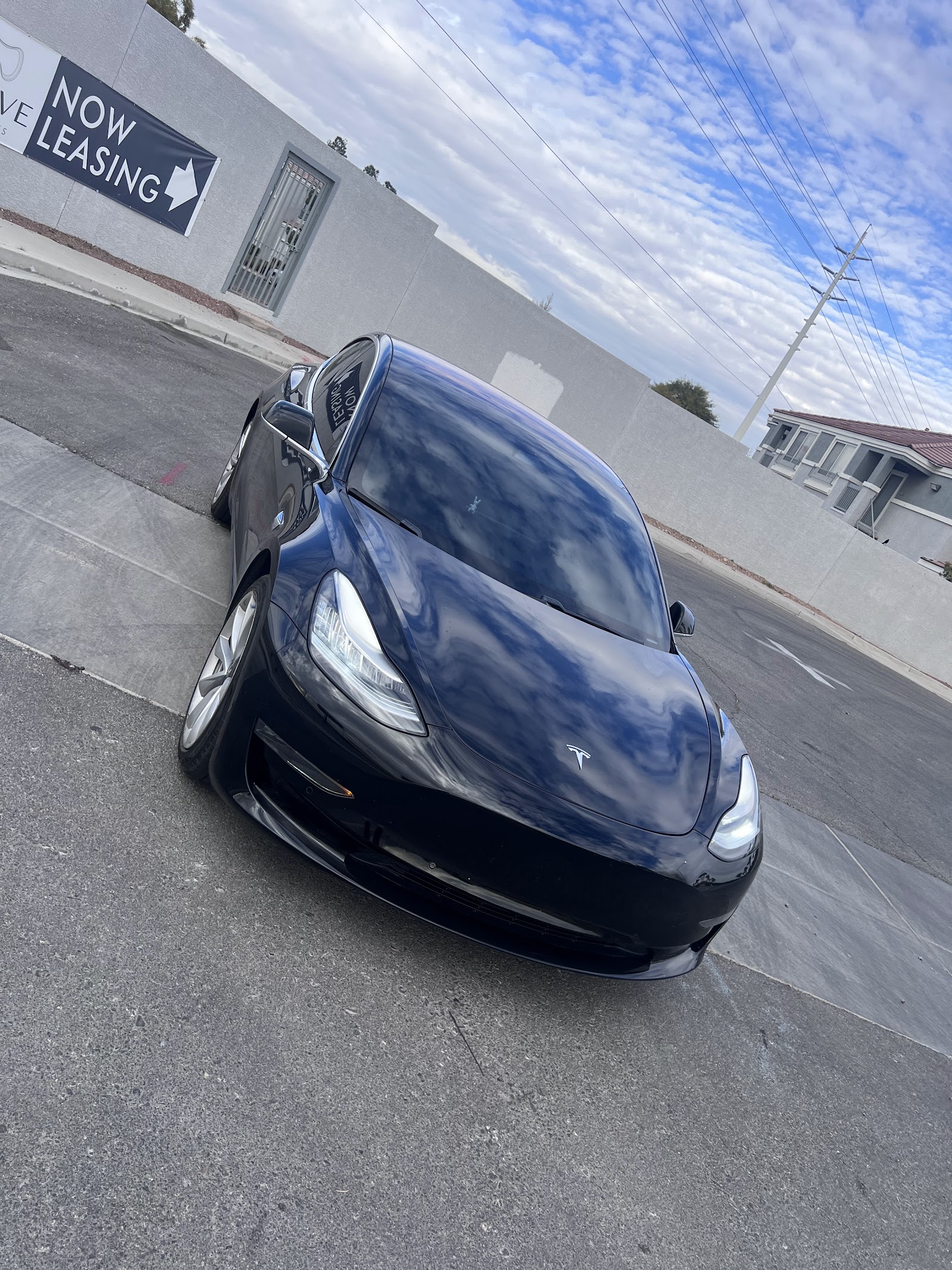 Black Tesla Model 3 with freshly tinted windows parked outdoors under a blue sky